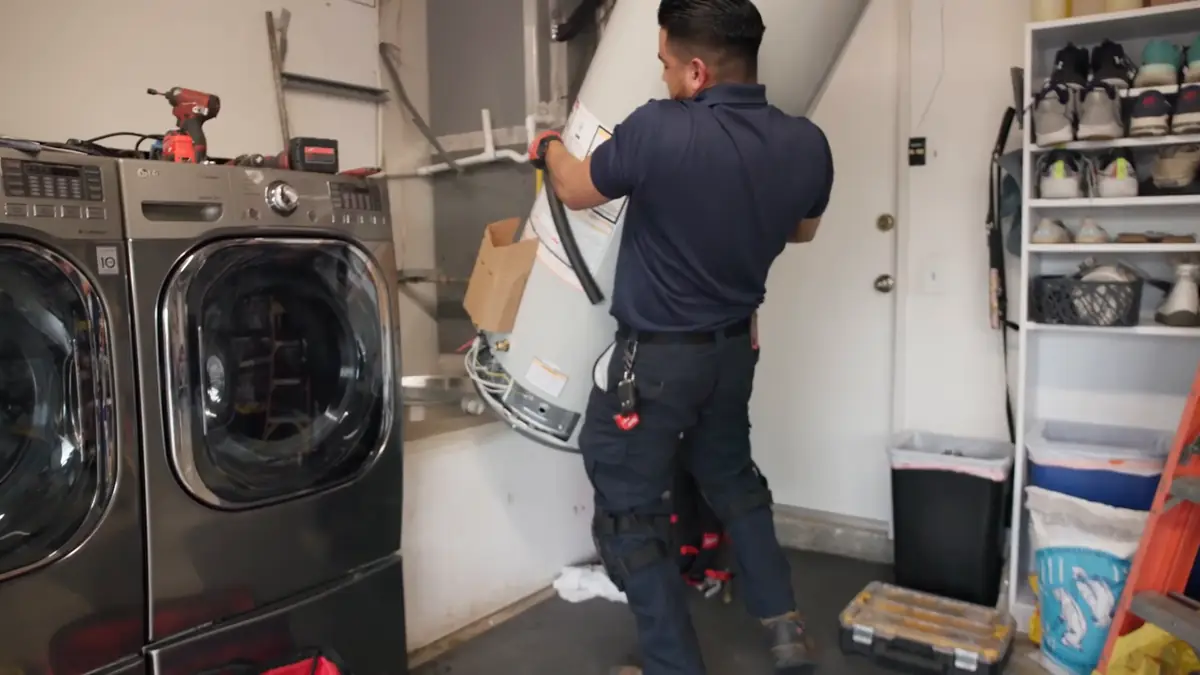 A Water Heater Man technician removing an old tank water heater from a garage