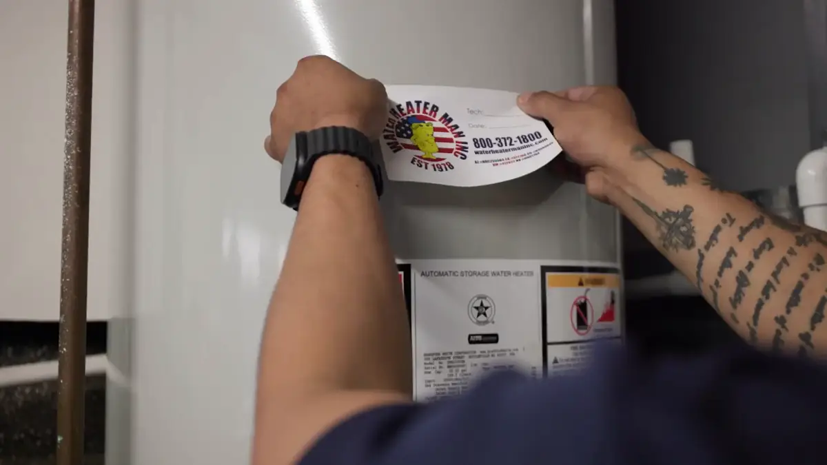 A Water Heater Man service sticker being placed on a newly installed water heater
